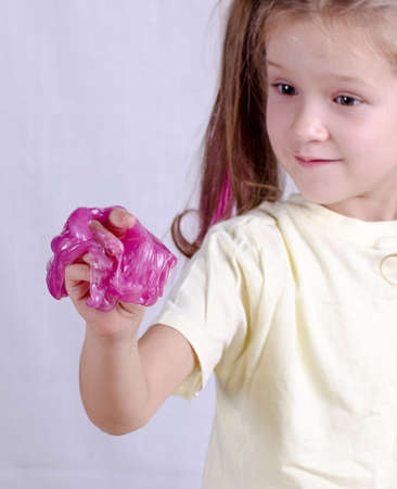 Adorable caucasian little girl holding slime toy, worldwide popular self made toy. Kid playing with slime squeeze and stretching it.の写真素材