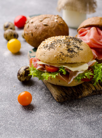 Delicious crispy burger bun with sliced ham on a vintage wooden cutting board. Dark moody food photo...