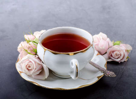 Romantic Tea time backdrop with vintage white porcelain tea cup, gentle pink roses on a dark gray background.の写真素材