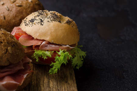 Delicious crispy burger bun with sliced ham on a vintage wooden cutting board. Dark moody food photo good for bar menu and posters.の写真素材