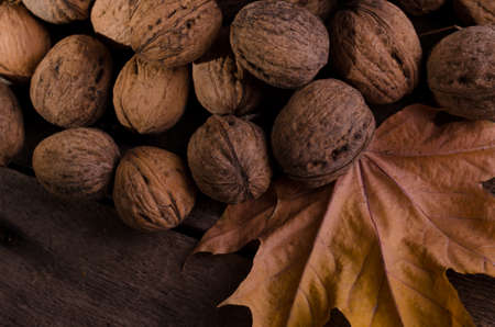 Autumnal rural frame with plenty of dry walnuts and yellow maple leaf on an old wooden background.の写真素材