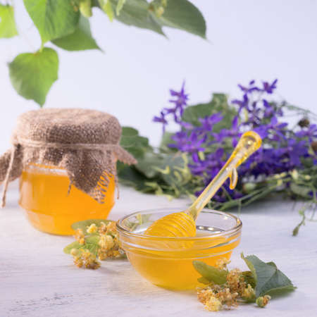 Linden Honey in Jar and bowl with a honey dipper on a white wooden table. Defocused branch of linden in the foreground.の写真素材