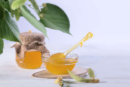 Linden Honey in Jar and bowl with a honey dipper on a white wooden table. Defocused branch of linden in the foreground.の写真素材