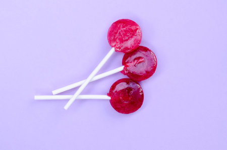 Three Red Lollipops on a Violet Color Background. Top View Flat Lay Background.