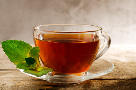 Cup of hot mint tea with fresh green juicy mint leaves. Aromatic tea in a glass cup on vintage...