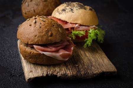 Delicious crispy burger bun with sliced ham on a vintage wooden cutting board. Dark moody food photo good for bar menu and posters.の写真素材
