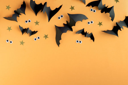 Halloween frame template with black paper bats and plastic spooky eyes on a colored yellow...