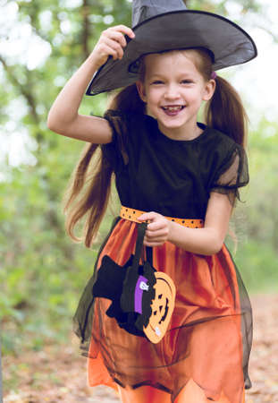 Happy little girl wearing a witch carnival costume and basket for sweets running to trick or treat outdoor.の写真素材