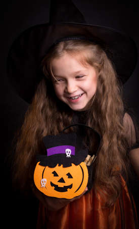 Happy laughing little girl wearing a witch carnival costume playing with basket for treats. Child girl Halloween kid against a black background.の写真素材