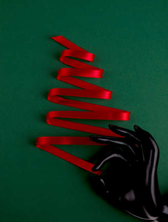 Christmas tree made from silk red ribbon and plastic mannequin hand on a bright green backdrop. Merry Christmas and Happy New Year festive background with empty space for text.の写真素材