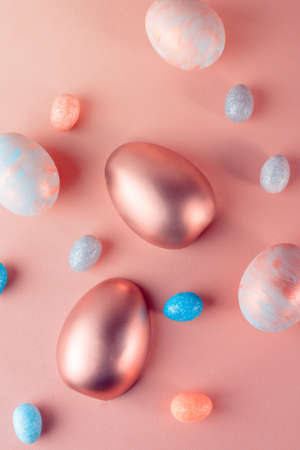 Trendy Easter background with Gold and colored Easter eggs on a light coral color background with copy space for text. Top view flat lay still life. Easter concept.の写真素材