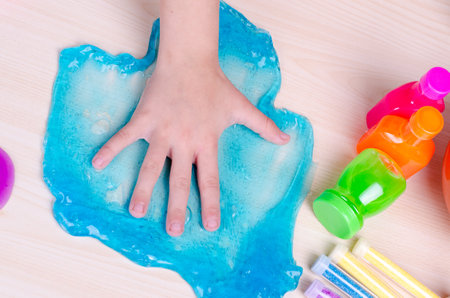 Kid's hand smashed bright blue slime on the table. Top-Down image of child hand and slimes, worldwide popular toy.の写真素材