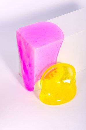 Slime, bright pink and yellow elastic toys flow down of white box, against white background.の写真素材