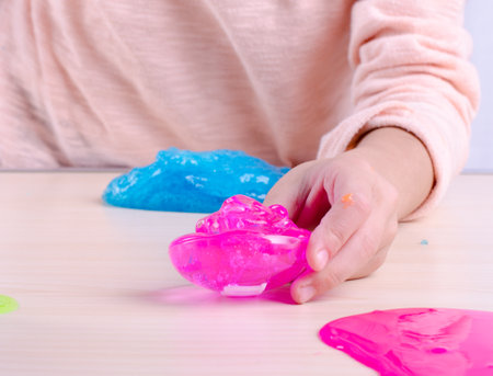 Toy Slime in a kids hand. Little girl playing with bright pink stretching slime. worldwide popular self made toy. Making slime by yourself.の写真素材