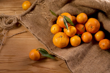 Fresh juicy tangerines or mandarins with green leaves on sack cloth and wooden table. Winter seasonal fruitsの写真素材
