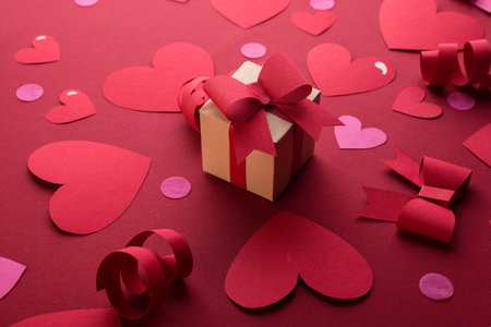 Happy st. Valentines day concept with craft paper gift box, red paper hearts, bows against dark red background with space for text.の写真素材