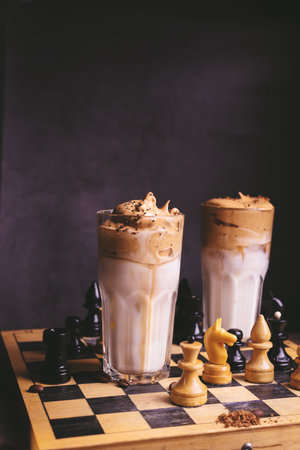 Dalgona Coffee. Whipped icing drink with instant coffee popular in Korea Creamy cocktail in tall Glasses decorated with chess on wooden chessboardの写真素材