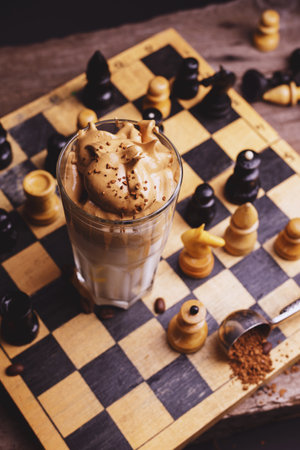 Dalgona Coffee. Whipped icing drink with instant coffee popular in Korea Creamy cocktail in tall Glasses decorated with chess on wooden chessboardの写真素材
