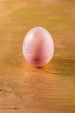 Easter egg colored in pink and gold on an old wooden cracked golden surface.の写真素材