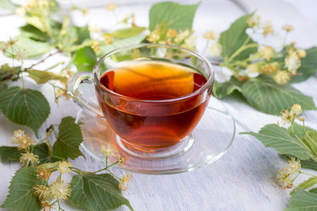 Glass cup of linden tea, and linden flowers on a white wooden table. Healthcare hot drink.の写真素材