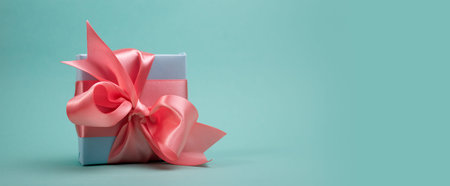 Banner with beautiful Gift box tied with a pink ribbon on ae Turquoise Background. Good for Easter...