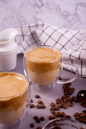 Dalgona Coffee. Whipped icing drink with instant coffee popular in Korea Creamy cocktail in a transparent double wall glass mug against the grey backgroundの写真素材