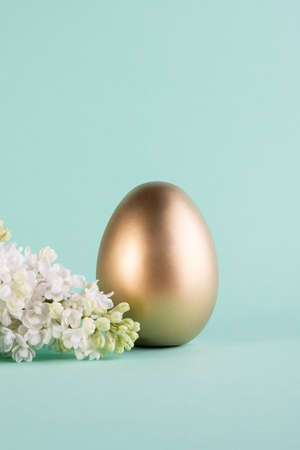 Easter Festive banner with big decotrative gold egg, lilac blossom on a light blue background and copy space for text.の写真素材