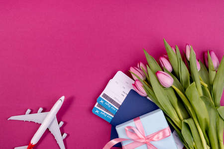 Romantic travel concept with gentle tulips boarding pass documents, little gift box and airplane model against pink color backgroundの写真素材