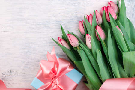 Romantic gift box tied with big pink bow and spring tulips on white wooden surface. Mothers day or Easter holiday minimalist concept.の写真素材