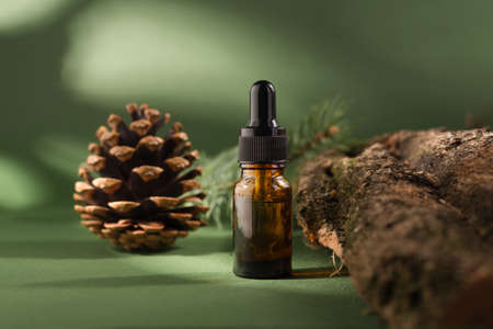 Cosmetic bottle with dropper on a wooden bark and moss. Pine tree essential oils on a dark green background.の写真素材