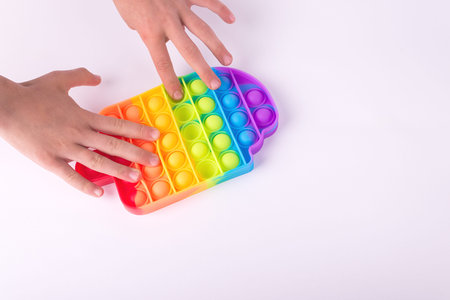 Childrens hand playing with rainbow fidget toy pop it isolated on the white.