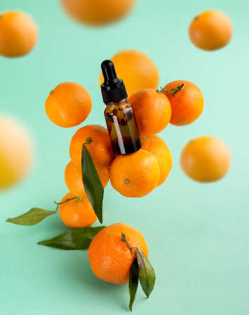 Bottle of Essential Oil of Mandarin among ripe tangerines flying in the air. Cosmetics oil in aromatherapy and Healthcare.の写真素材