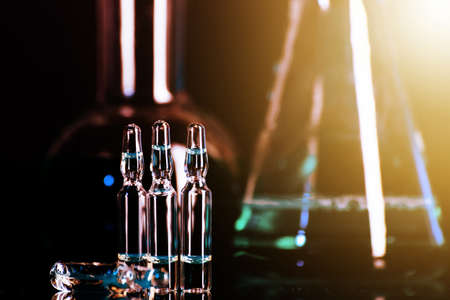 Glass ampoules with liquid for injection against laboratory flasks on dark background.の写真素材