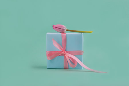 Beautiful pink tulip levitating on a turquoise color gift box tied with silk bow. Minimalist trendy still life.の写真素材