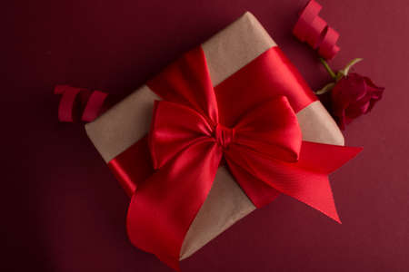 Close up Gift box with red silk bow against dark purple background. Valentines day romantic gift box with red rose. 14 February background.の写真素材