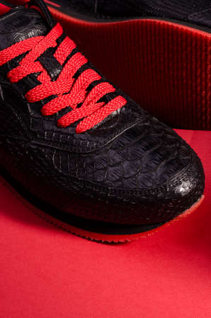 Fashionable snakeskin leather sneakers. Black sneakers with bright red bootlaces against a black and red background.の写真素材