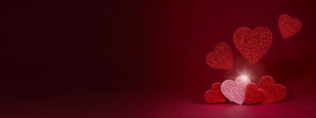 Valentines day concept banner with sparkling glitter hearts against abstract red background and the bokeh of garland with space for text.の写真素材