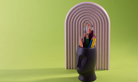 Multi Colored Pencils are placed in Vase Face Form Against a Green.