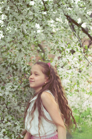 Adorable 9 years old girl with long curly hair surrounded by plenty branches blossoming of white spring flowers.の写真素材