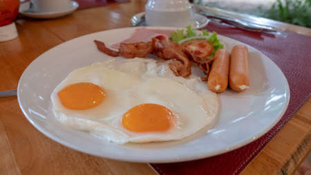 closeup fried egg, sausage and ham on white plateの写真素材