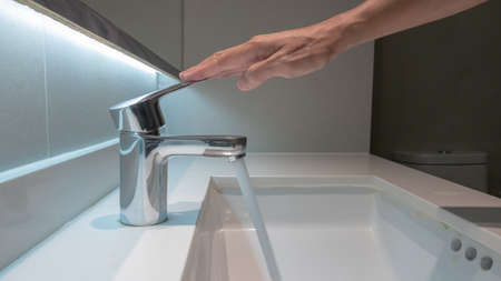 male hand turns off the water faucet in the bathroomの写真素材