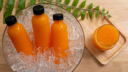top view glass of orange juice and bottle of orange juice in ice bucket with green leavesの写真素材