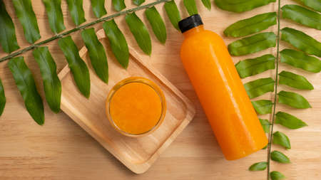 top view glass of orange juice and bottle of orange juice on wooden background with green leavesの写真素材