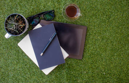 Casual work area with tablets, notebooks, mobile pens and a glass of tea on the grass.の写真素材