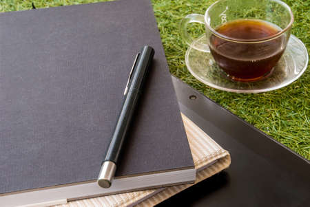 Casual work area with tablets, notebooks, mobile pens and a glass of tea on the grass.の写真素材