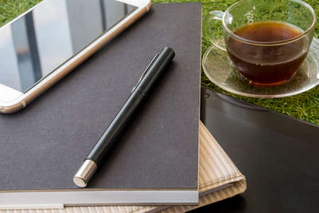 Casual work area with tablets, notebooks, mobile pens and a glass of tea on the grass.の写真素材