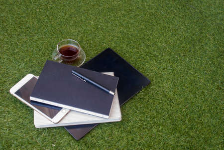 Casual work area with tablets, notebooks, mobile pens and a glass of tea on the grass.の写真素材