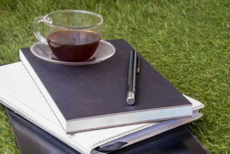 Workspace with tablets A pen, a notebook, and a cup of tea on a comfortable lawnの写真素材