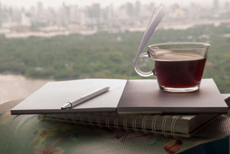 Hot coffee mug placed on a notebook to write a diary in the room overlooking the river in the morning.の写真素材