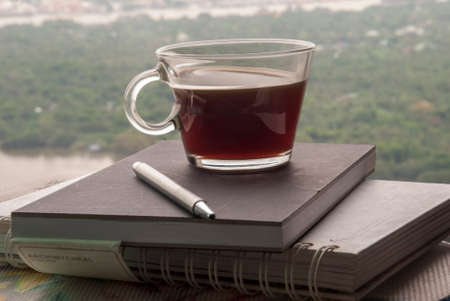 Hot coffee mug placed on a notebook to write a diary in the room overlooking the river in the morning.の写真素材